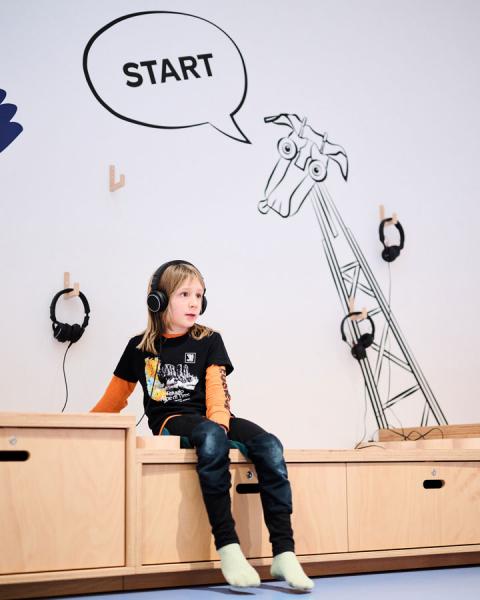 Child sitting on a piece of furniture with headphones.